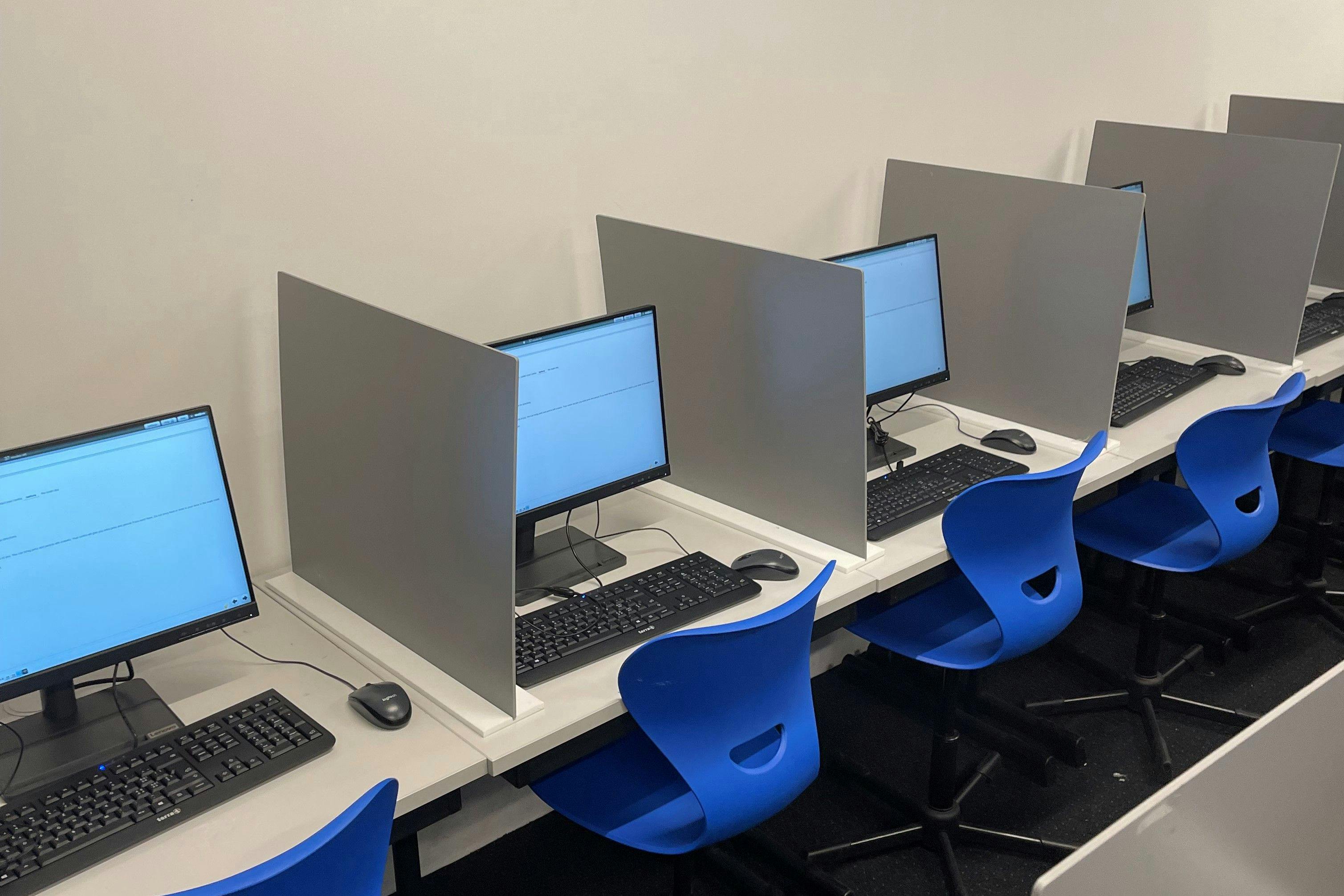 Four blue chairs in front of computers with keyborads, mouse and headphones. All computer are turned on for the tcf exam taking place in this exam room.